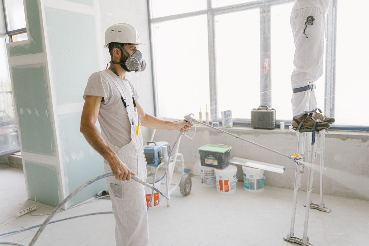 why-choose-us Two construction workers wearing protective gear and painting interior walls for a renovation project.