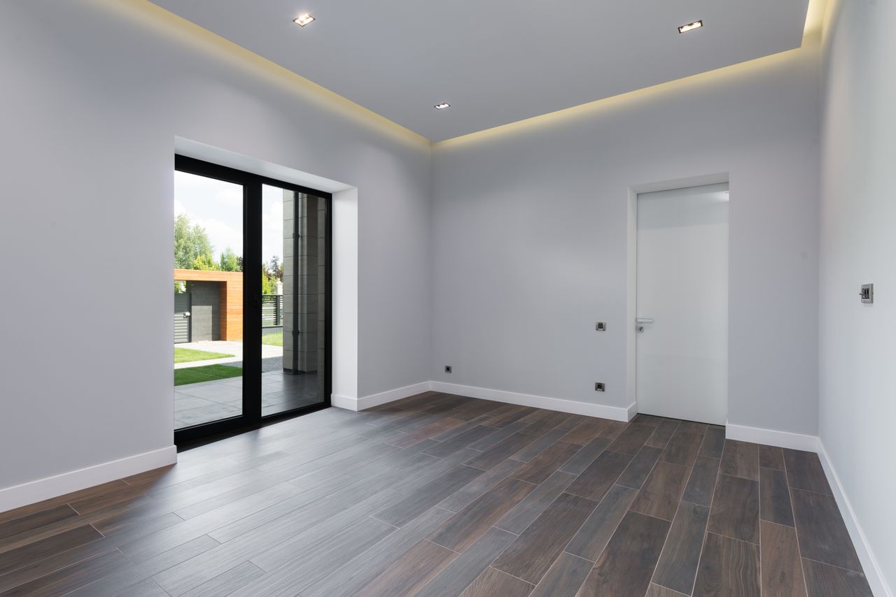 Interior of spacious room with laminate flooring big glass doors viewing terrace and white walls in daylight